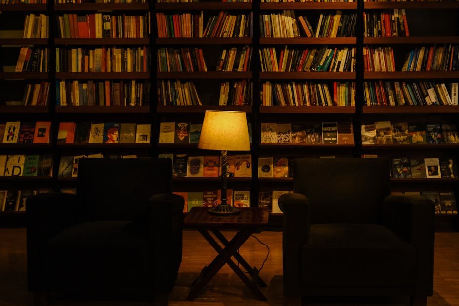 Wing chair beside a tall bookshelf in a low-lit study, the conversational interior this heretic review keeps returning to as the stage for the whole picture
