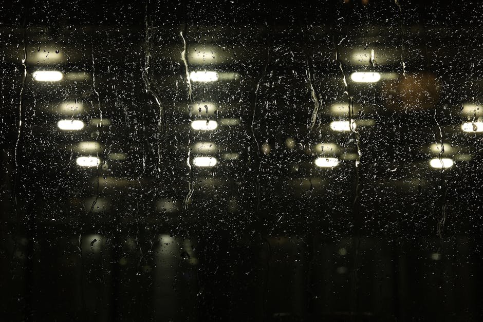 Rain-streaked window at night with a single lamp glowing inside, the atmospheric register a working heretic review uses to ground its craft observations